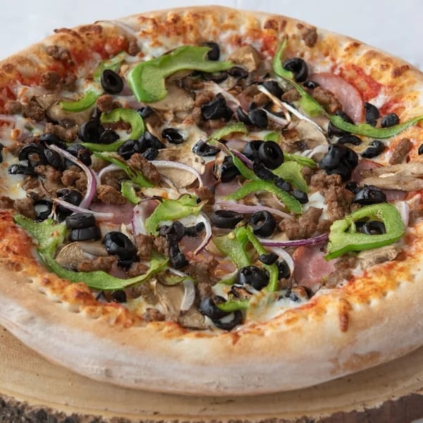 A whole pizza with green peppers, black olives, sausage, mushrooms, and onions on a wooden board.
