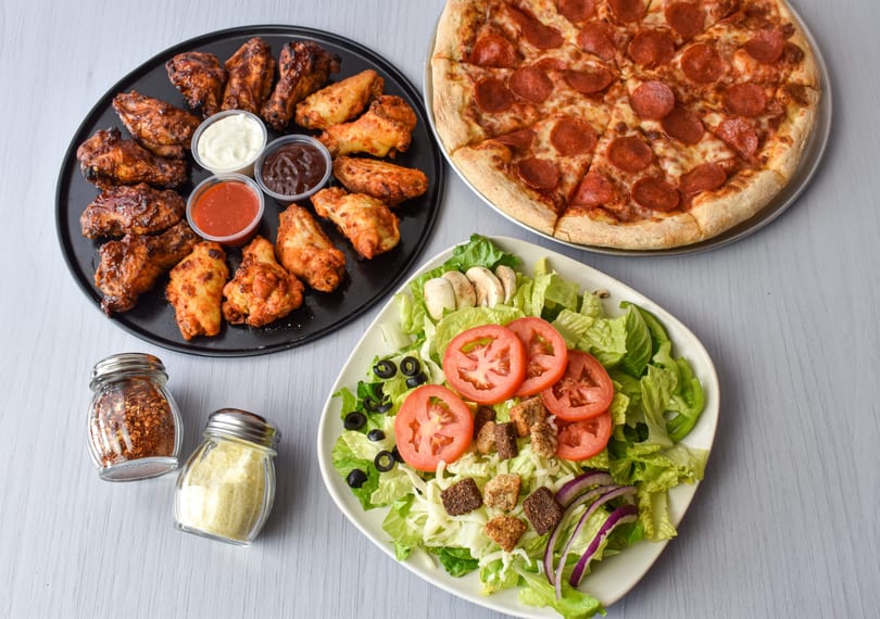 A pepperoni pizza, a platter of chicken wings with dipping sauces, and a fresh garden salad.