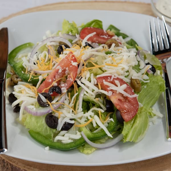 A fresh garden salad with lettuce, tomatoes, olives, onions, green peppers, and shredded cheese.