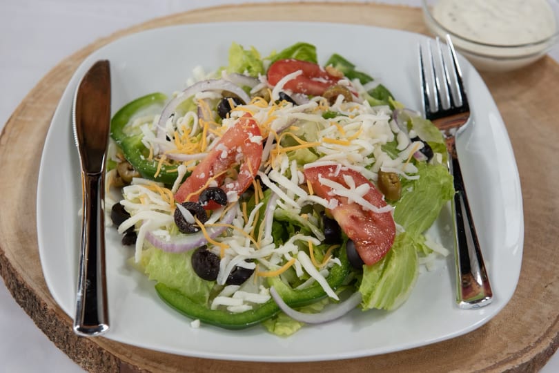 A fresh garden salad with lettuce, tomatoes, olives, onions, green peppers, and shredded cheese.