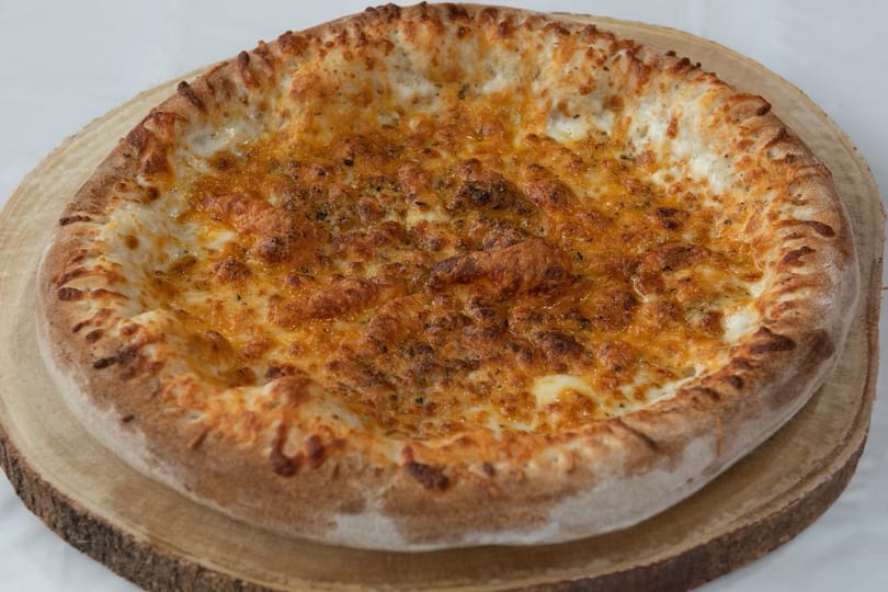 A golden-brown cheese pizza with a thick crust, topped with herbs, on a wooden board.