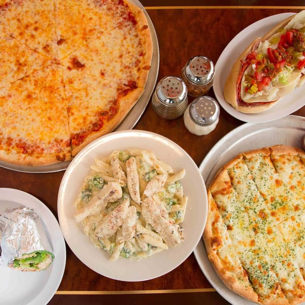A table laden with a cheese pizza, a sub sandwich, chicken alfredo pasta, garlic knots, and a wrap.