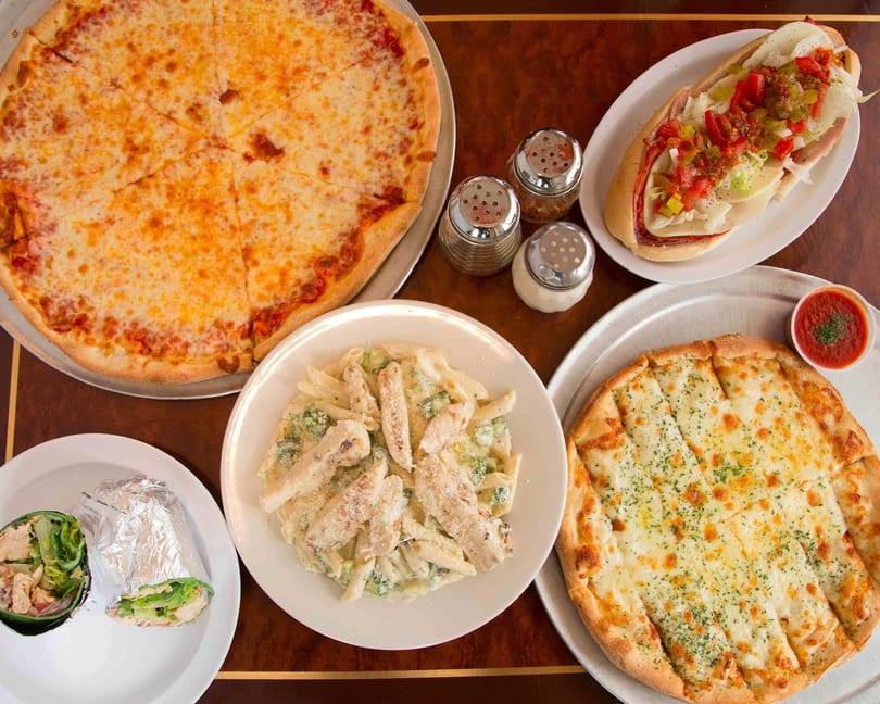 A table laden with a cheese pizza, a sub sandwich, chicken alfredo pasta, garlic knots, and a wrap.