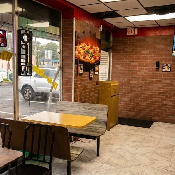 Interior of a casual restaurant with brick walls, tables, and a large window looking out onto a parking lot.
