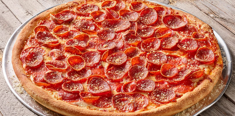 A large, round pepperoni pizza with a thick crust, sprinkled with parmesan cheese, on a metal pan.